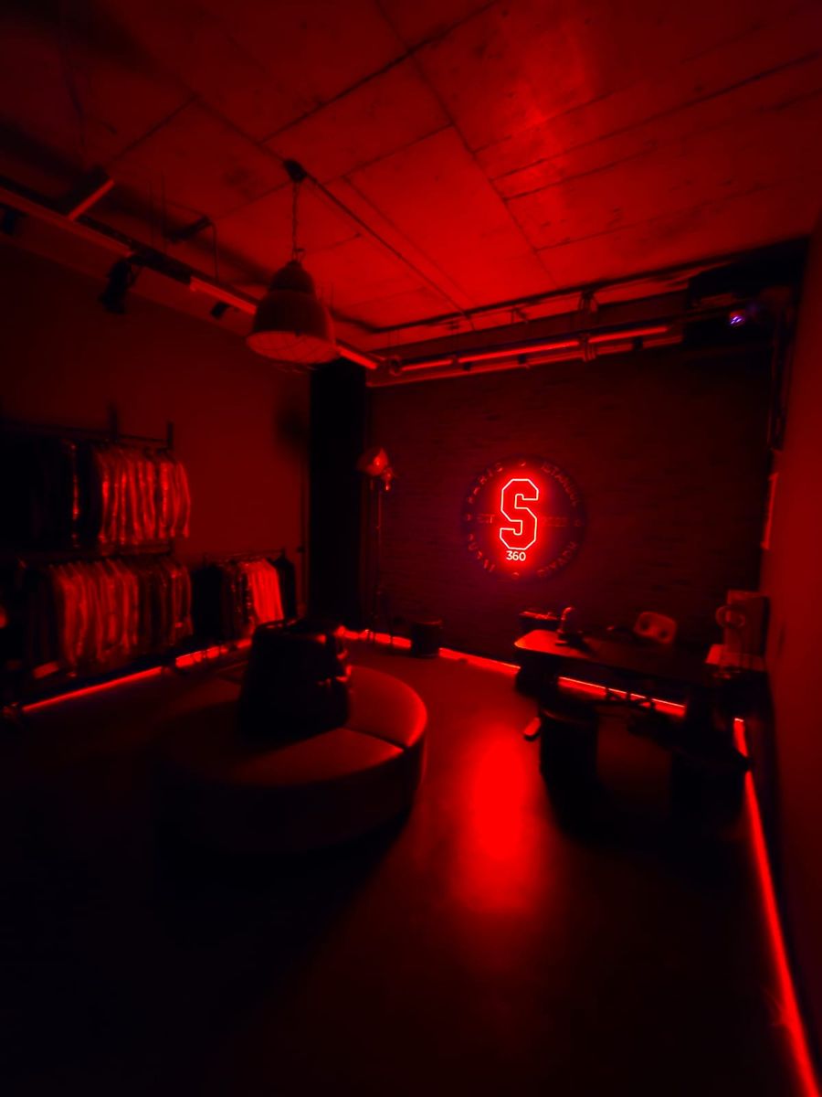 Showroom bathed in red light, with garment rails and the neon S on the wall
