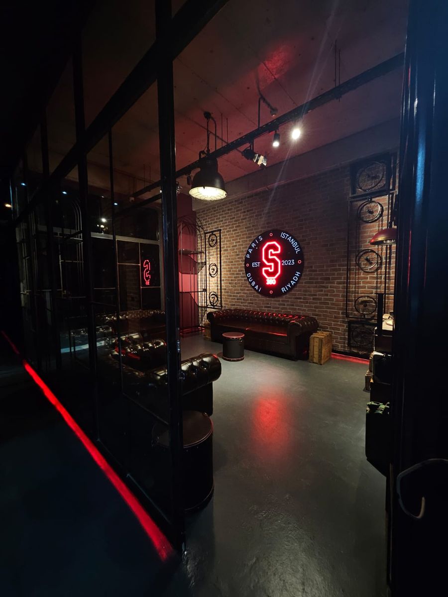 The lounge seen through a glass partition, with a leather sofa and the neon sign
