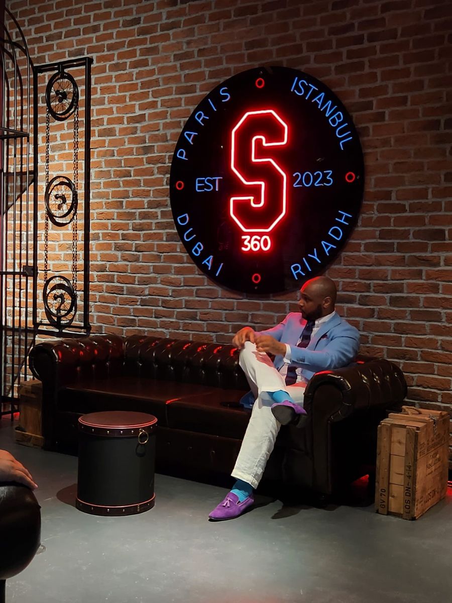 Leather chesterfield sofa against a brick wall under the neon S360 sign
