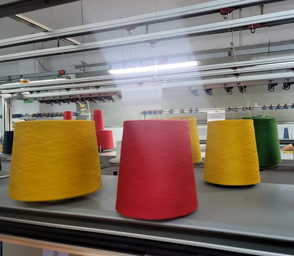 Big cones of yellow, red and green yarn lined up on a knitting machine