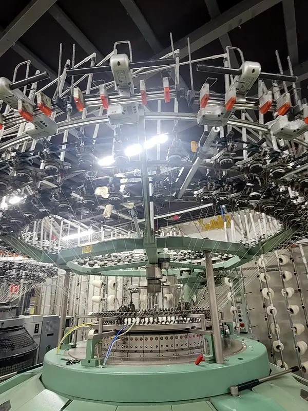Looking up into a circular knitting machine with dozens of yarn feeds
