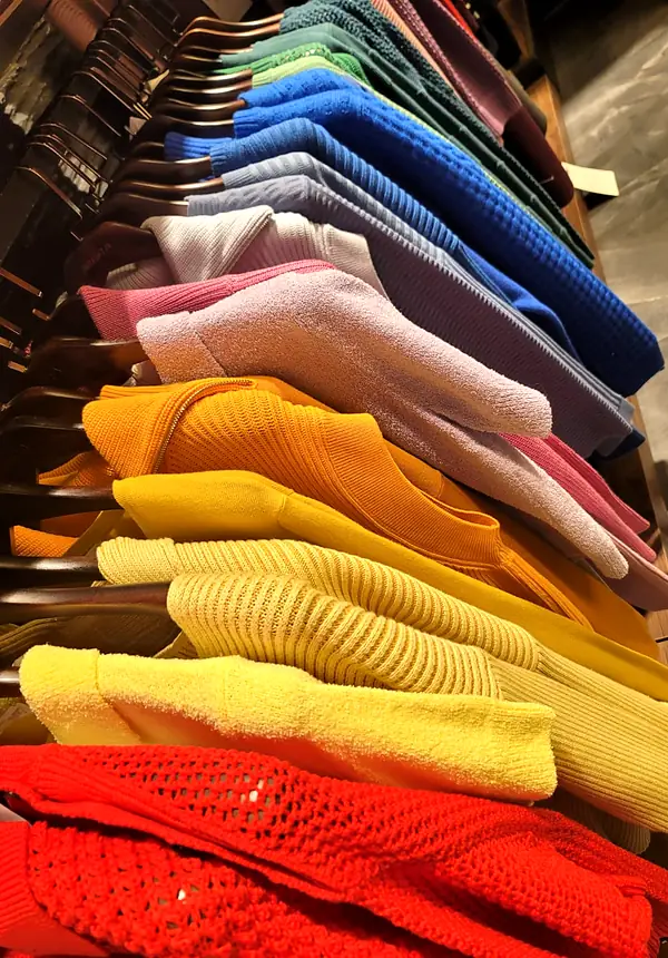 Knit sweaters on hangers running from green and blue through pink, yellow and red