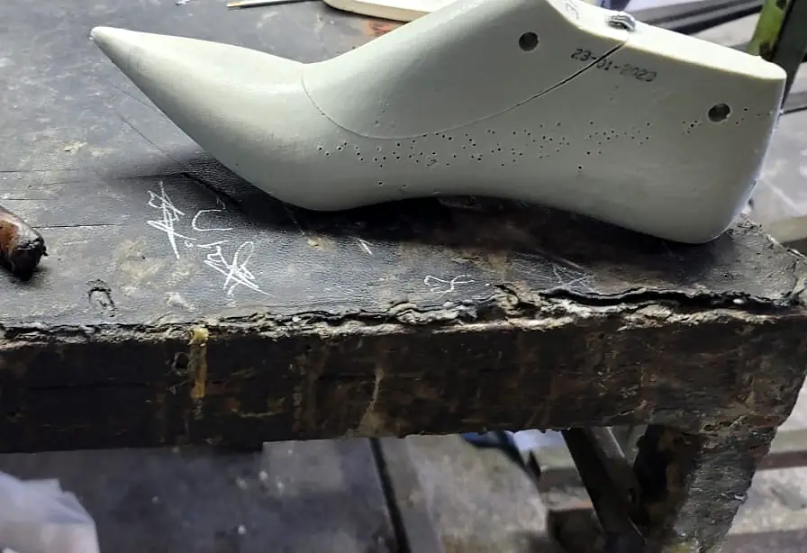 Pale grey pointed shoe last on a worn workbench next to pliers