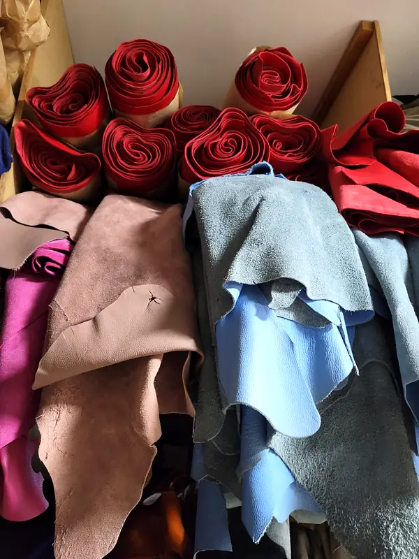 Red leather rolls on top of loose grey, blue, pink and brown hides