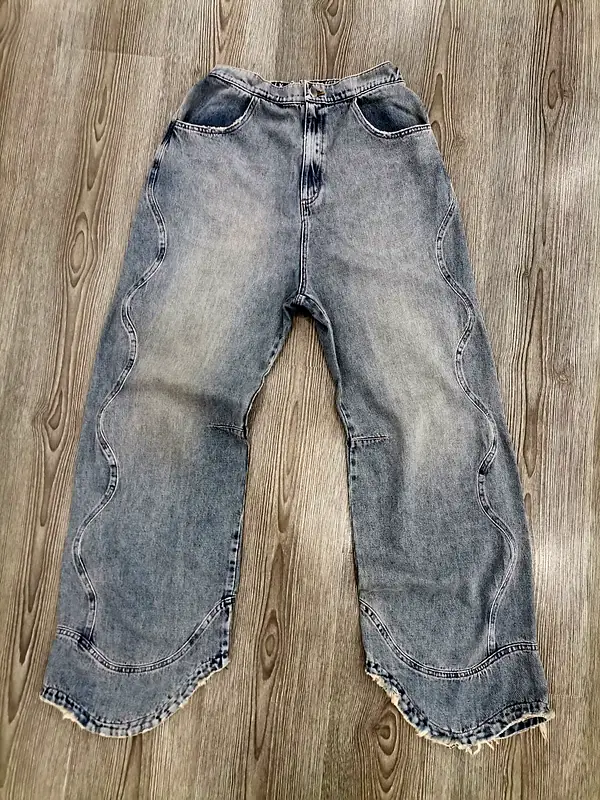 Light-wash wide-leg jeans with wavy side seams and raw scalloped hems, laid flat