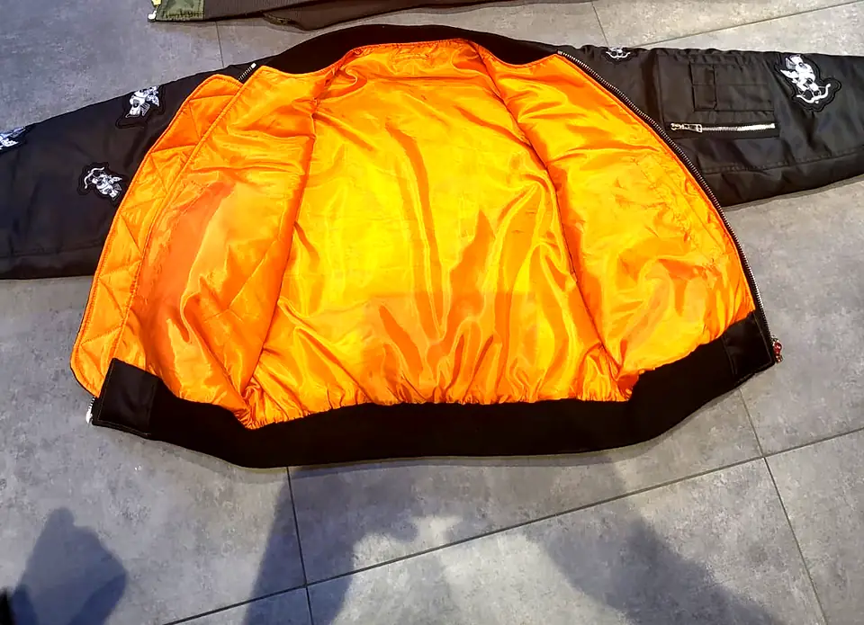 Black bomber jacket laid open to show its bright orange quilted lining