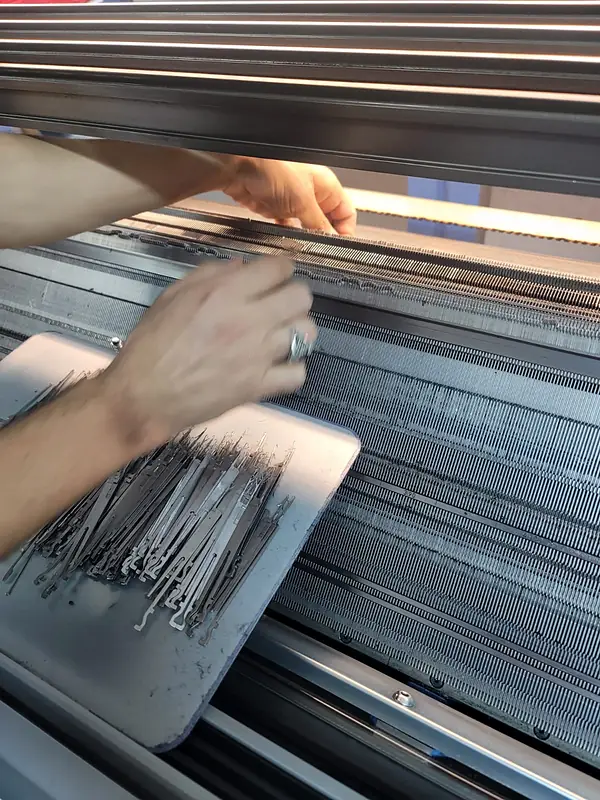 Hands changing needles on the needle bed of a flat knitting machine