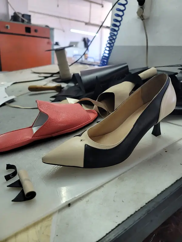 Cream and black pointed pump on a workbench beside cut leather pieces