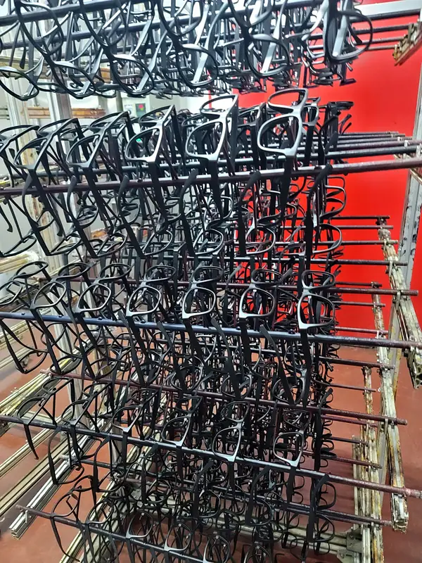 Rows of black glasses frames hanging on a metal drying rack