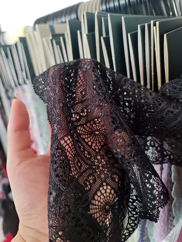 A hand holding up black stretch lace in front of a rack of samples
