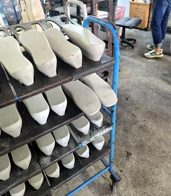 Rack of pale shoe lasts on a blue trolley in the workshop