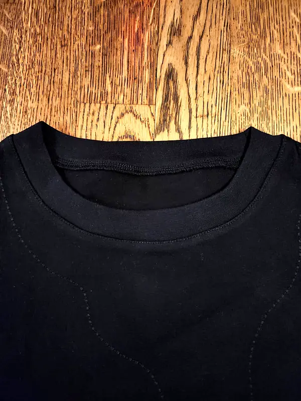 Close-up of the neckline of a black T-shirt laid on a wooden floor