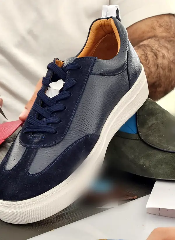 Navy leather and suede sneaker with a white sole, scissors and leather swatches around it