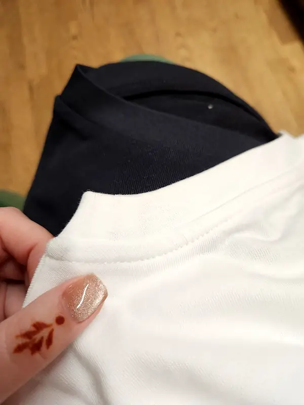 A hand folding back the collar of a white T-shirt over a navy one