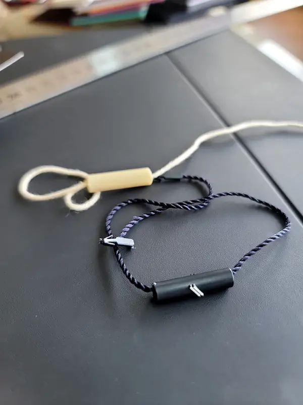 Two hang-tag cords, one cream and one navy, with plastic toggles on a dark table