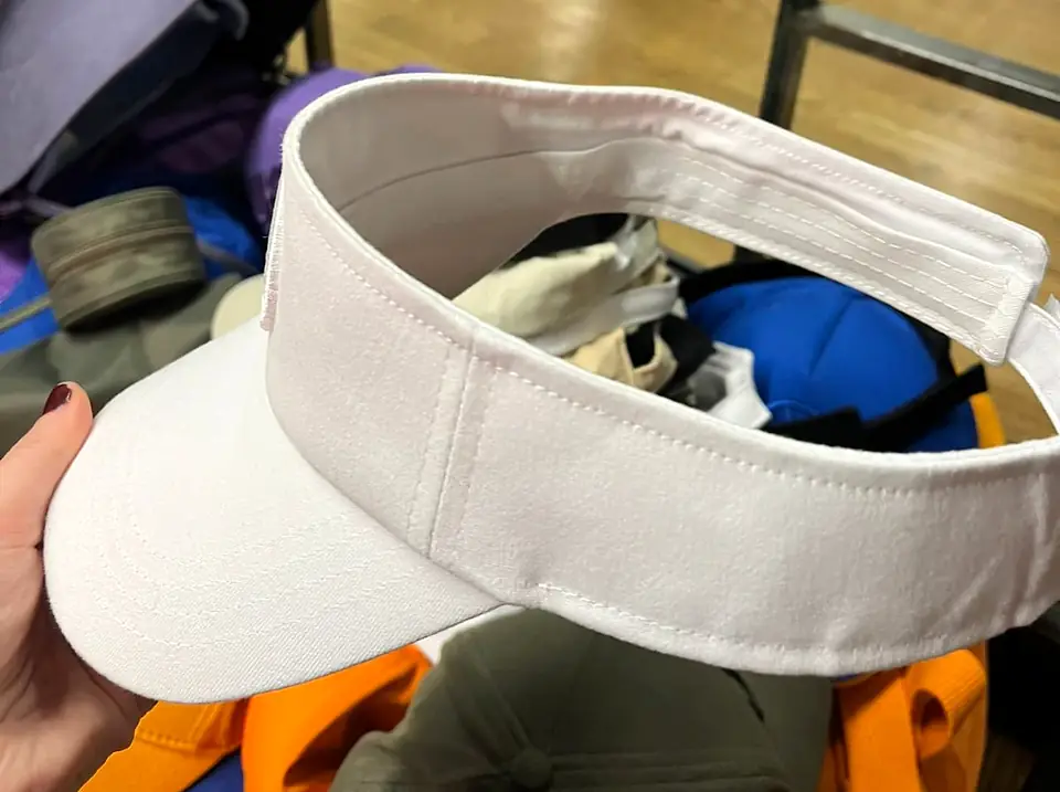 A hand holding a white cotton twill sun visor with a strap at the back