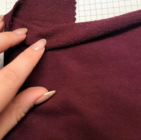 Fingers turning back a burgundy cotton fleece to show its looped reverse