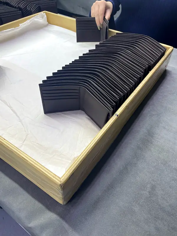 A tray of dark brown bifold wallets standing in a row, one lifted out for checking
